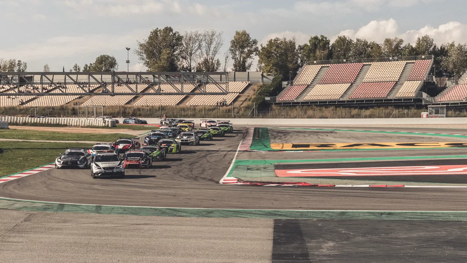 Départ d'une course : le peloton groupé derrière la voiture de sécurité devant les tribunes